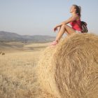 A young woman enjoying a peaceful moment on a hay bale in a sunny countryside field.