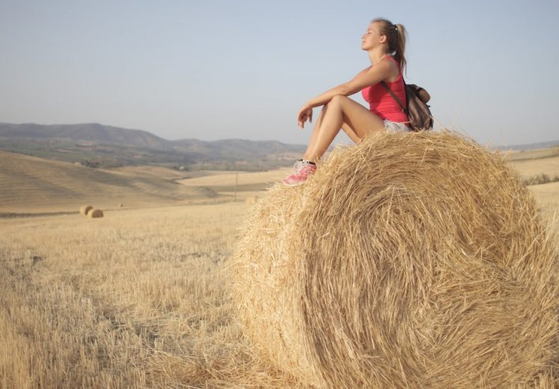 A young woman enjoying a peaceful moment on a hay bale in a sunny countryside field.
