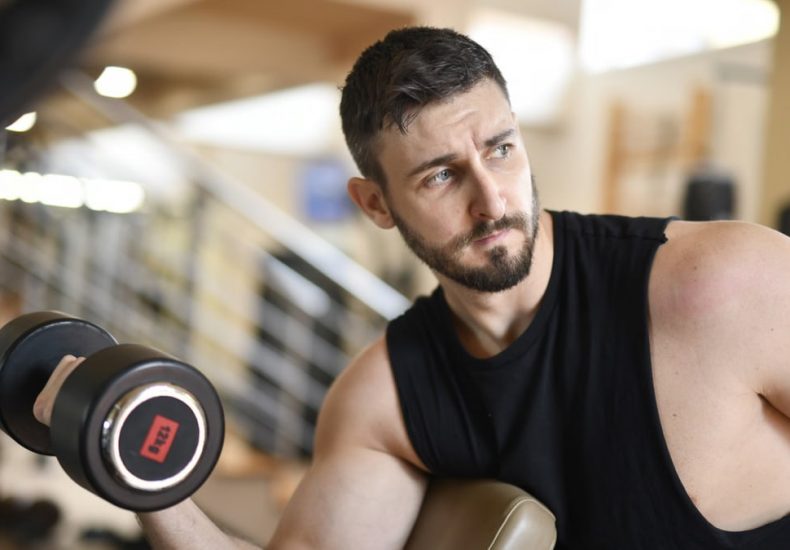 A determined man lifting a dumbbell indoors, showcasing strength and fitness.